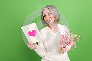 Photo of optimistic good mood smiling senior lady hold reading her greeting card happy valentine day isolated on green