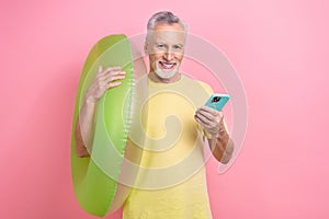 Photo of optimistic handsome man with beard dressed yellow t-shirt hold inflatable lifesaver smartphone isolated on pink