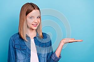 Photo of optimistic little blond girl hold empty space wear jeans jacket isolated on blue color background