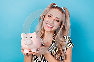 Photo of optimistic toothy beaming girl dressed striped blouse hands hold piggy bank saving money isolated on blue color