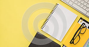 Photo overhead of notebook glasses paperclips clipboard keyboard and folder isolated on the yellow background
