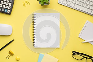 Photo overhead of notebook keyboard calculator pen computer mouse notes plant glasses and paperclips isolated bright color yellow
