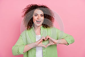 Photo of overjoyed woman with perming coiffure dressed shirt hands showing heart astonished staring isolated on pink