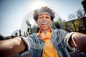 Photo of overjoyed youngster dressed jeans jacket with headphones on neck making selfie recording video on frontal