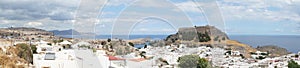 Photo panorama. View of the white buildings of Captains houses and the ancient Acropolis of Lindos in August.