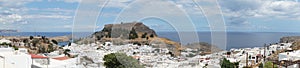 Photo panorama. View of the white buildings of Captains houses and the ancient Acropolis of Lindos in August.