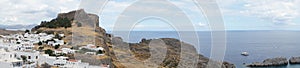 Photo panorama. View of the white buildings of Captains houses and the ancient Acropolis of Lindos in August.