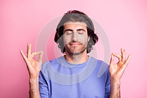 Photo of peaceful relaxed young man make om sign meditate wear purple sweater isolated on pastel pink color background