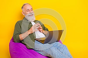 Photo of pensioner man sit beanbag hold computer look screen wear green shirt isolated yellow color background