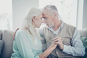 Photo of perfect aged pair leaning foreheads holding hands posing family portrait sitting cozy sofa indoors