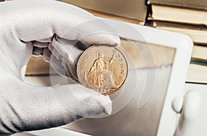 Photo of a person\'s hand in gloves holding a british coin