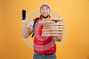 Photo of pizza man receives orders from customers via smart phone, holds many carton boxes with fast food, has unpleasant look to