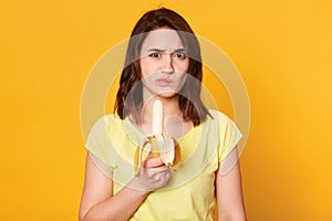 Photo of pleasant looking woman in casual clothes, ready for eating fresh banana, does not like this fruit, has unpleasent facial photo