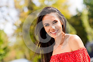 Photo portrait of adorable brunette in red clothes with off-shoulders spending free time in green park in spring smiling