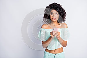 Photo portrait of afraid woman holding phone in two hands biting lip looking at blank space isolated on white colored