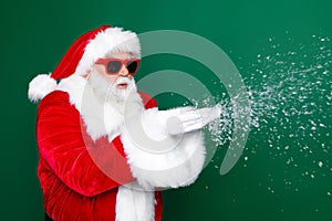 Photo portrait of aged senior man blowing snowy wear trendy santa claus costume coat isolated on green color background