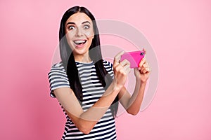Photo portrait of amazed girl with open mouth holding phone in two hands vertically isolated on pastel pink colored