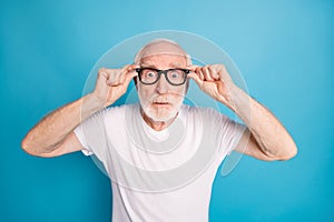 Photo portrait of amazed old man putting on glasses isolated on pastel blue colored background