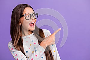 Photo portrait of amazed small girl in glasses pointing at empty space smiling advicing isolated on vibrant purple color