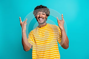 Photo portrait of attractive young man wink show rock horns sign dressed stylish striped yellow clothes isolated on cyan