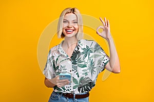 Photo portrait of attractive young woman gadget show okey symbol dressed stylish leaves print clothes isolated on yellow