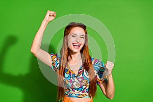 Photo portrait of attractive young woman raise fists winning dressed stylish retro clothes  on green color