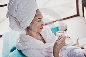 Photo portrait of attractive young woman sit sofa enjoy hold drink tea cup head wrapped towel dressed bath robe home