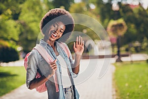 Photo portrait of black skinned pretty girl with curly hair smiling greeting waving hand keeping backpack wearing denim