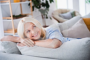 Photo portrait of charming retired woman sit sofa charming smile look empty space stylish home decor living room modern