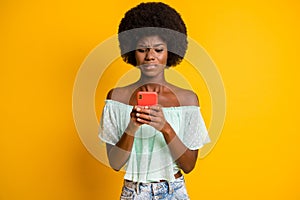 Photo portrait of confused woman biting lower lip holding phone in two hands isolated on vivid yellow colored background