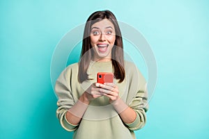 Photo portrait of crazy screaming girl holding phone in two hands isolated on vivid cyan colored background