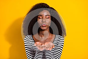 Photo portrait of curly girl in striped shirt sending air kiss with pouted lips isolated vibrant yellow color background