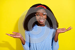 Photo portrait of curly girl wearing headband glasses smiling not know shrugging shoulders isolated vibrant yellow color