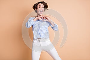 Photo portrait of cute girl showing heart on chest with hands isolated on pastel beige colored background