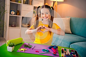 Photo portrait of cute small girl play sculpt plasticine show heart gesture hands dressed stylish yellow clothes modern