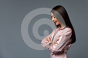 Photo Portrait of a cute woman girl with dark hair in pink clothes on a gray background in the studio. She says, shows