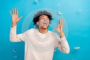 Photo portrait of cute young guy have fun look falling feathers afro hair dressed white pajama outfit isolated on blue