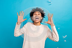 Photo portrait of cute young guy look up feathers raise hands excited wear trendy white pajama outfit isolated on blue