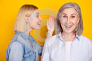 Photo portrait of daughter telling secret to her mother smiling isolated vivid yellow color background