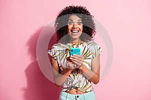 Photo portrait of excited girl holding phone in two hands isolated on pastel pink colored background