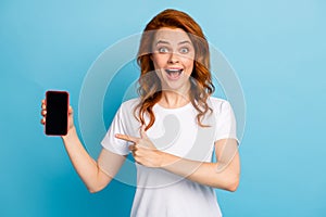 Photo portrait of excited girl pointing finger at phone with blank display space isolated on pastel blue colored