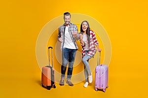 Photo portrait full body view of celebrating couple with suitcases isolated on vivid yellow colored background