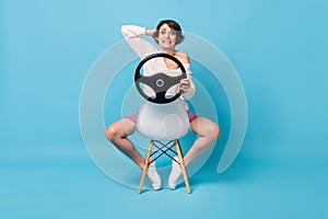 Photo portrait full body view of scared woman holding steering wheel sitting on reversed chair isolated on pastel blue