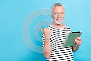 Photo portrait of funny old male hold ebook look point empty space wear trendy striped garment isolated on blue color