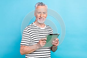 Photo portrait of funny old male hold tablet reading ebook dressed stylish striped garment isolated on blue color