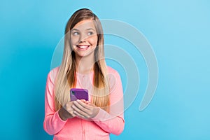 Photo portrait of girl holding phone in two hands looking at blank space isolated on pastel blue colored background