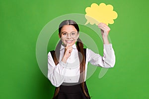 Photo portrait of girl holding yellow thought bubble card touching chin isolated on vivid green colored background