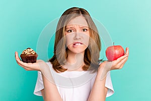 Photo portrait girl scaling sweet cupcake apple biting lip sad keeping diet isolated vivid teal color background