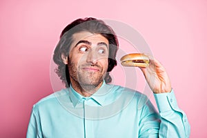 Photo portrait of guy holding cheeseburger in one hand looking at it in temptation isolated on pastel pink colored