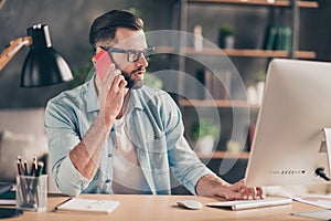 Photo portrait of guy talking on phone working on pc at table in modern industrial office indoors